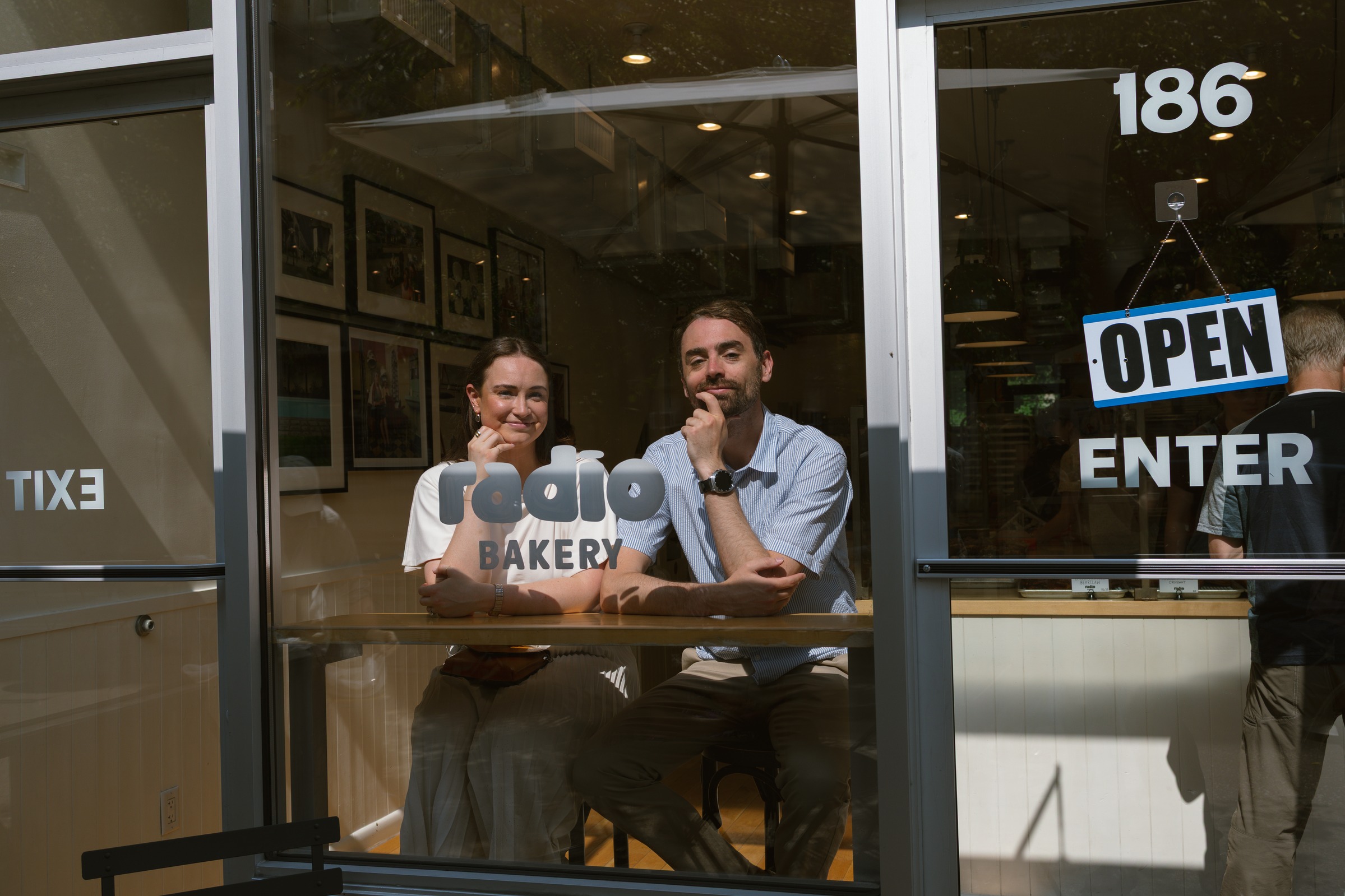 Monika and Haggai seen through the window of Radio Bakery, leaning on the counter with their chins in their hands.